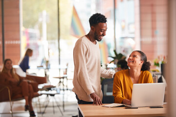Businessman And Businesswoman Having Informal Meeting By Desk In Modern Open Plan Office