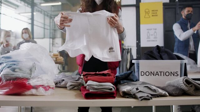 Volunteers sorting out donated clothes in community charity donation center, coronavirus concept.