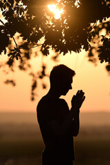 Closeup portrait young man praying against sunset