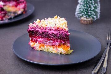 Herring salad under a fur coat. Traditional Russian multilayered salad from herring, beets, potatoes, carrots and eggs. Small Christmas tree. Close-up, grey background.