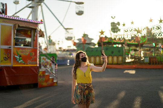 Mujer joven positiva en vestido de verano haciendo selfie y divirti&eacute;ndose en el parque de atracciones