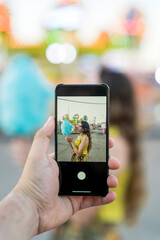 Mujer joven atractiva en vestido de verano haciendo un selfie en el parque de atracciones visto a través de la cámara del smarpthone