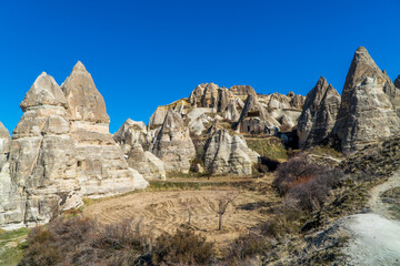 Fototapeta na wymiar Beautiful panorama view of a field and caves inside typical rock formations and fairy chimneys in Cappadocia, Turkey