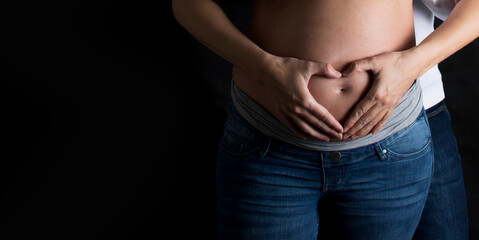 Pregnancy belly and woman hands. Couple and maternity on black background. Panorama banner with copy space.