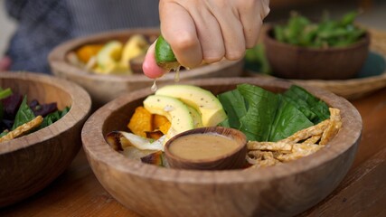 Close up of hand squeezing a lime over a healthy green salad with tofu and avocado. Preparing a...