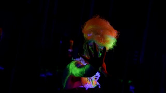 female dancer with fluorescent makeup and neon hairstyle is dancing in darkness