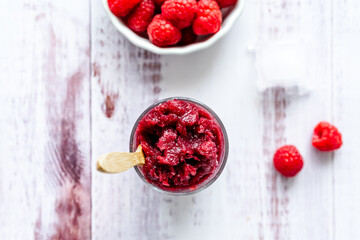 Frozen Eis mit Himbeeren in einem Glas und frische rote Beeren auf einem weißen Holz Tisch. Draufsicht, Sommer Erfrischung.