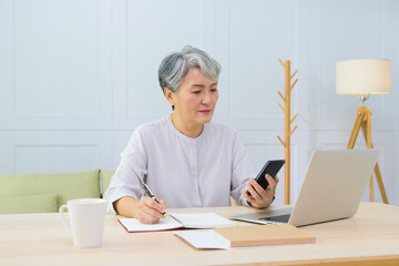 Senior Asia woman working from home using laptop and checking message on smart phone.
