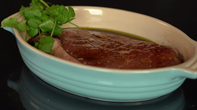 4K slide by of fresh steak marinating in blue dish with cilantro on the side. Indoors, kitchen.