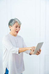 Smiling middle-aged Asia woman browsing wireless Internet on tablet at home, happy modern senior female using pad device, elderly technology concept.