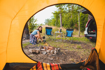 view from camping tent woman cooking on burner near bonfire