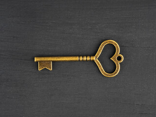 Bronze antique key with heart shaped hole on black wooden background