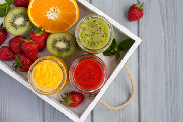 Top view of  fruit smoothies or puree in the small glass jars on the white tray on the gray wooden  background. Copy space.