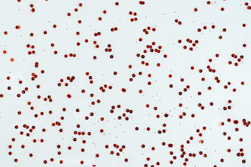 Red metallic shiny sequins are chaotically scattered on a white background. Wallpaper. Horizontal photo. Abstract background. 