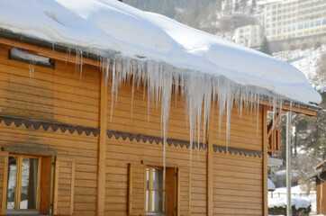 Ice dams on wooden cabin house roof during winter