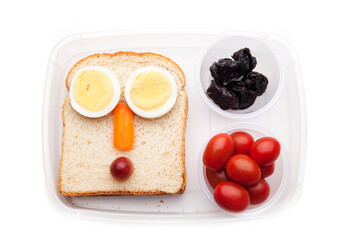 School lunch box snacks for kids over white background. Back to school. Healthy and fun snacks options for parents. Food art creative concepts. Bows with fruits and vegetables and cute face sandwich.