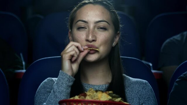 A young woman eating nachos at the movie theater.