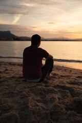 Man sitting on the seashore watching the sunset. He is sitting on the sand. The sea is calm. Mediterranean, Denia