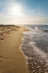 Beach of golden sand and blue sea. The sea is calm with small waves. The sky is blue. Uncrowded landscape.