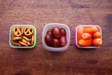 School lunch box snacks for kids over wooden background. Back to school. Healthy and fun snacks options for moms. Cute food art creative concepts. Bows with fruits and vegetables.