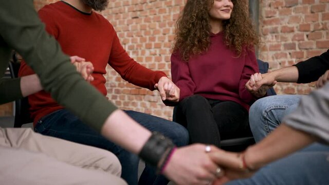 Group of people on therapy session, members holding each other by hand.