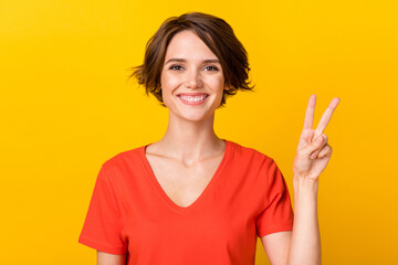 Photo satisfied young lady toothy smile look camera fingers show v -sign isolated on yellow color background