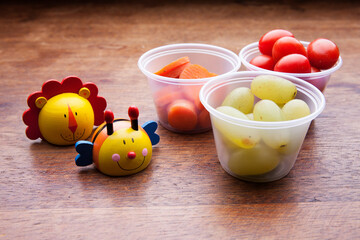 School lunch box snacks for kids over wooden background. Back to school. Healthy and fun snacks options for moms. Cute food art creative concepts. Bows with fruits and vegetables.