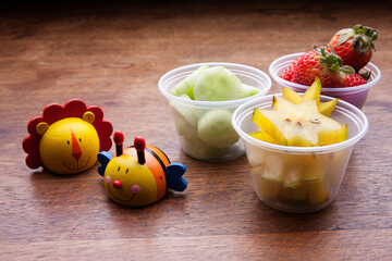 School lunch box snacks for kids over wooden background. Back to school. Healthy and fun snacks options for moms. Cute food art creative concepts. Bows with fruits and vegetables.
