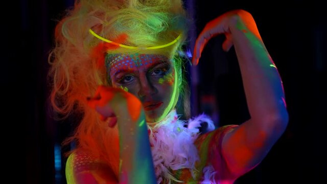 young model with ultraviolet paint on face and body, posing in darkness, moving hands slowly