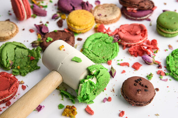 Crushed macaroon of different colors on a white background with a hammer..