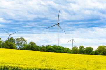 Windräder vor wolkigem Himmel mit gelben Rapsfeld im Vordergrund / Wind turbines against cloudy sky with yellow rape field in foreground