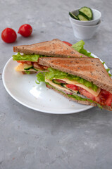 Delicious sandwich with fresh lettuce leaves, tomatoes, cucumbers and cheese on a grey table background.