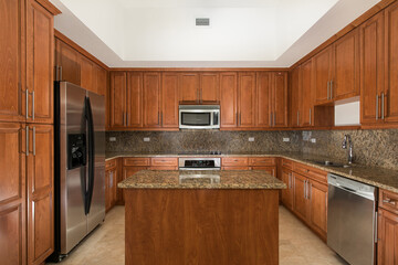 Fototapeta premium Vacant Kitchen with cherry wood cabinets and center island with granite.