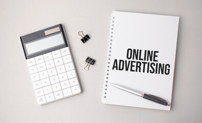 The word online advertising is written on a white background next to a pen ,calculator and reports. Business concept