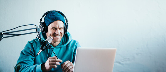 Cheerful host streaming his audio podcast at small and cozy home broadcast studio