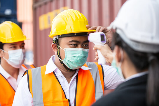 Female worker scanning fever temperature with digital thermometer to construction site staff wearing hygiene face mask protect from Coronavirus or COVID-19. New Normal working