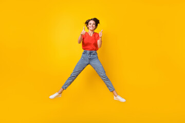 Fototapeta na wymiar Full size photo of optimistic brunette short hairdo lady jump show ok sign wear t-shirt jeans sneakers isolated on yellow background