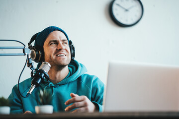 Cheerful host streaming his audio podcast at small and cozy home broadcast studio