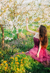 Portrait of a luxury girl under a flowering tree. A young girl in purple dress against the background of spring blooming cherry trees. 