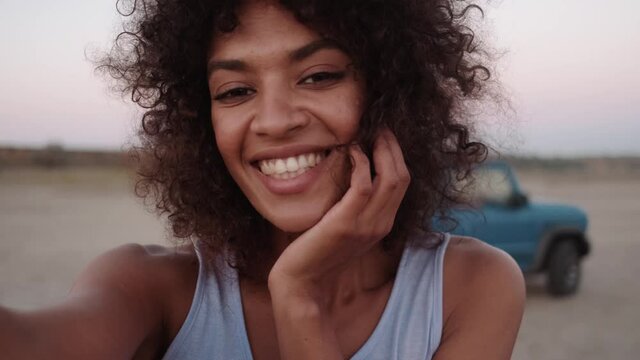 The close-up view of the African smiling woman waving at the camera and showing to the car in the nature