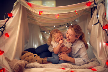 Laughing Mother And Young Daughter Having Fun In Homemade Camp In Child's Bedroom At Home