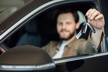 Happy man showing a car key inside his new vehicle, focus on hand. Male customer with car key sitting in new modern car.