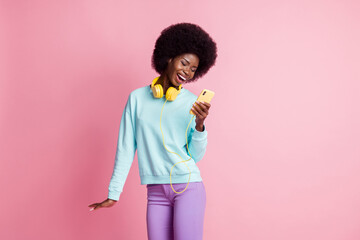 Photo portrait of girl keeping cellphone wearing headphones laughing isolated on pastel pink color background