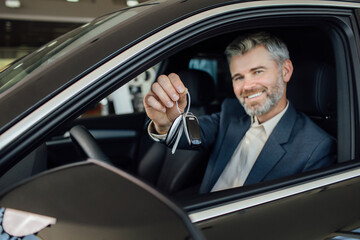 Happy man showing a car key inside his new vehicle, focus on hand. Male customer with car key...
