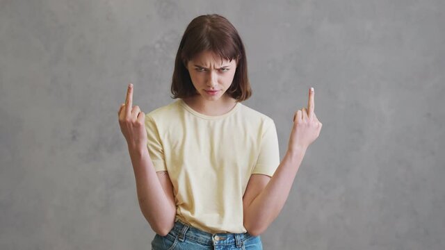The angry girl with short hair showing a middle finger to the camera while standing in the grey studio