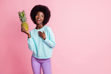 Photo of nice happy dark skin young woman hold pineapple look empty space hand chest isolated on pink color background