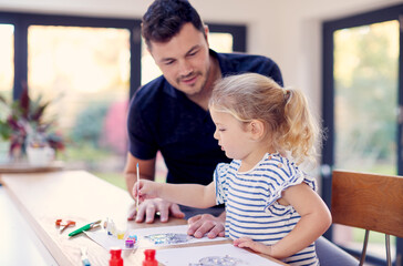 Father And Young Daughter Having Fun Doing Craft On Table At Home Together