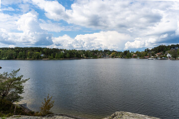 Amazing Panorama of the Baltic Sea Bay on sunny spring day. Rocky shores of Scandinavia covered with evergreen forests. Traditional Swedish wooden villas houses on the coast. Blue sky white clouds.