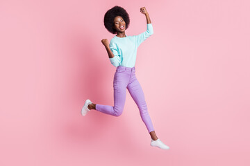 Full length photo of lucky cute dark skin lady wear colorful clothes rising fists jumping high isolated pink color background