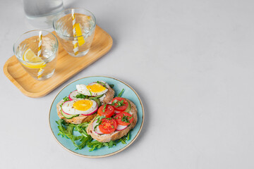 Toasted sandwiches white bread with cream cheese, vegetables: cherry tomatoes, cucumbers, eggs, parsley. Healthy vegetarian breakfast idea. Served with fresh lemon water, light background, copy space
